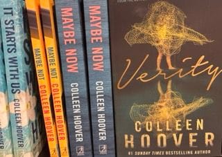 A bookshelf featuring several novels by Colleen Hoover, with the thriller Verity prominently displayed in the foreground. The dark cover of Verity shows a golden, abstract female figure, emphasising its psychological depth. This book explores Antisocial Personality Disorder (ASPD) through its chilling protagonist, who manipulates and deceives those around her while hiding behind charm and success.