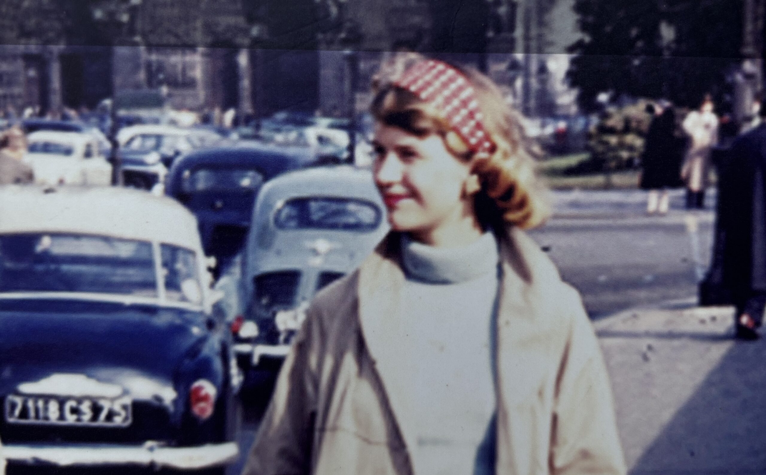 Vintage 1950s photograph of a young woman in a headscarf standing near classic cars, evoking the era of Sylvia Plath's Lady Lazarus and themes of depression in women's literature.